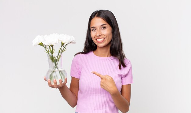 Młoda latynoska kobieta uśmiecha się radośnie, czuje się szczęśliwa i wskazuje na bok trzymając ozdobne kwiaty