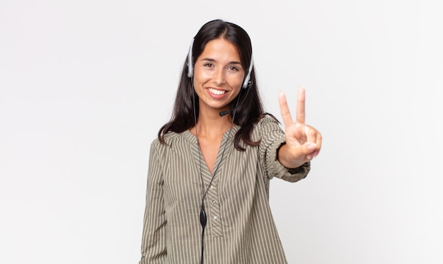Młoda latynoska kobieta uśmiechnięta i wyglądająca przyjaźnie, pokazująca numer dwa z zestawem słuchawkowym. koncepcja telemarketingu