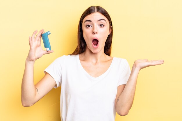 Zdjęcie młoda latynoska kobieta wyglądająca na zaskoczoną i zszokowaną, z opuszczoną szczęką trzymająca przedmiot. koncepcja astmy
