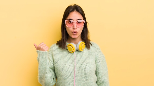 Młoda latynoska kobieta zdumiona w koncepcji słuchawek i okularów przeciwsłonecznych z niedowierzaniem