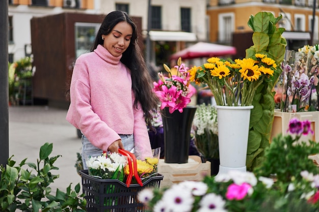 Młoda Latynoska kupuje rośliny, niosąc ich pełen kosz w ulicznej kwiaciarni