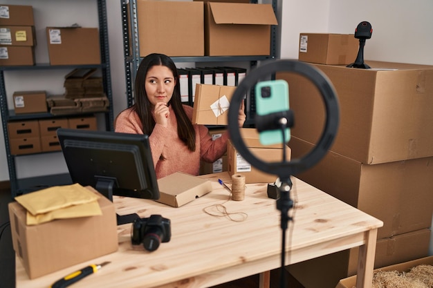 Młoda Latynoska pracująca w małej firmie e-commerce, nagrywająca wideo z poważną miną, myśląca o pytaniu z ręką na brodzie, zamyślona nad mylącym pomysłem