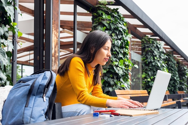 Młoda latynoska studentka z miejscowymi cechami używa swojego laptopa przy stoliku na zewnątrz