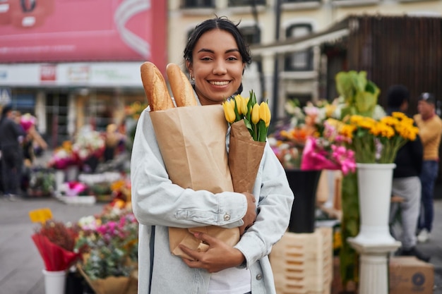Młoda Latynoska uśmiecha się, kupując żółte tulipany i chleb na straganie ulicznego sprzedawcy