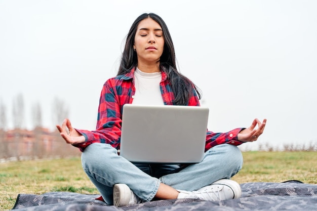 Młoda Latynoska z laptopem na nogach w pozycji medytacyjnej Latynoska kobieta z zamkniętymi oczami