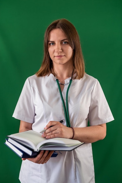Młoda lekarka z dużym szczerym uśmiechem trzyma książki w dłoniach portret odosobnionej pielęgniarki w jednolitej koncepcji opieki zdrowotnej