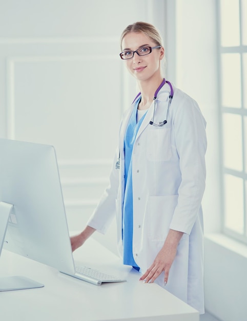 Młoda lekarz kobieta stojąca w pobliżu stołu na białym tle