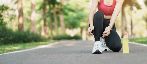 Młoda lekkoatletka wiąże buty do biegania z wodą Energy Drink, biegaczka gotowa do joggingu poza azjatą Fitness spacery i ćwiczenia w parku rano dobre samopoczucie i koncepcje sportowe