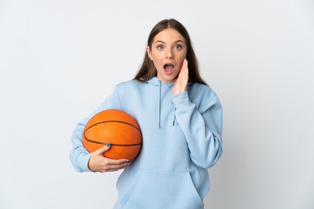 Młoda Litewska kobieta gra w koszykówkę na białym tle z zaskoczeniem i zszokowany wyraz twarzy
