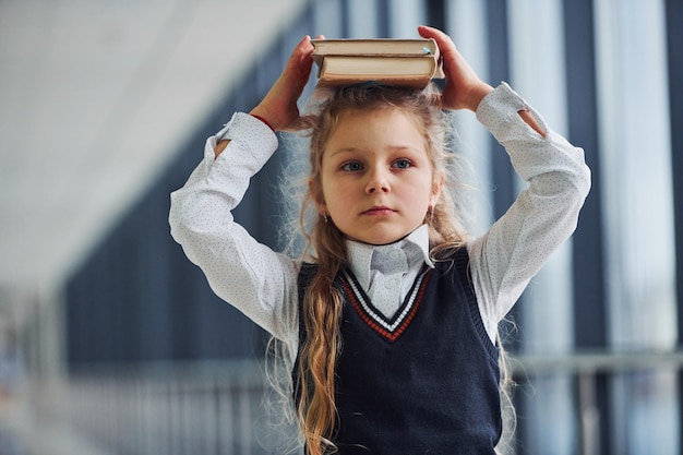Młoda mała uczennica w mundurze stojąca w korytarzu z książkami