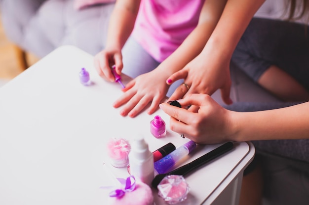 Młoda mama i córeczka robią manicure Mama i córka ubrane w różowe koszulki siedzą w pokoju