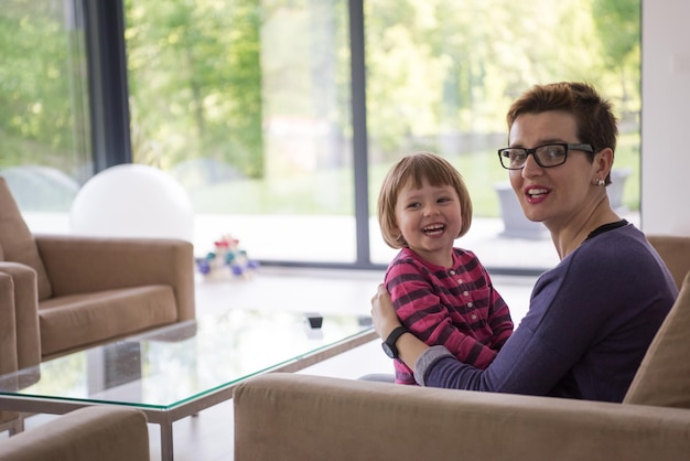 młoda mama i urocza dziewczynka cieszą się wolnym czasem przytulając się na kanapie w swojej luksusowej willi