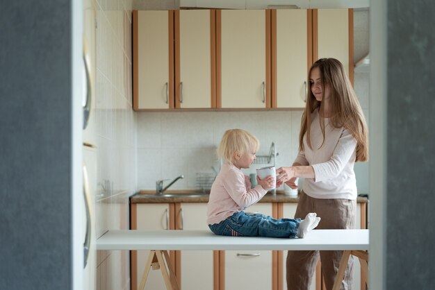 Młoda mama podaje w kuchni filiżankę mleka córeczce. Przyjemny poranek.