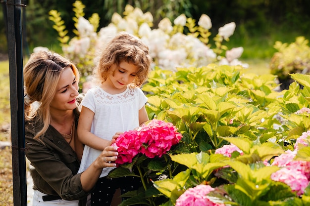 Młoda mama pokazuje swojej córeczce kwiaty hortensji w szklarni