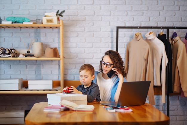 Młoda mama pracuje z małym chłopcem Kobieta biznesu rozmawia przez telefon i omawia problemy związane z pracą