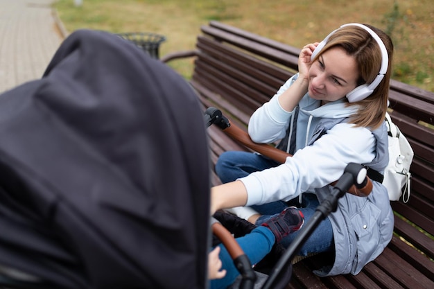 Młoda Mama Słucha Muzyki Na Słuchawkach Podczas Spaceru Z Wózkiem Dziecięcym