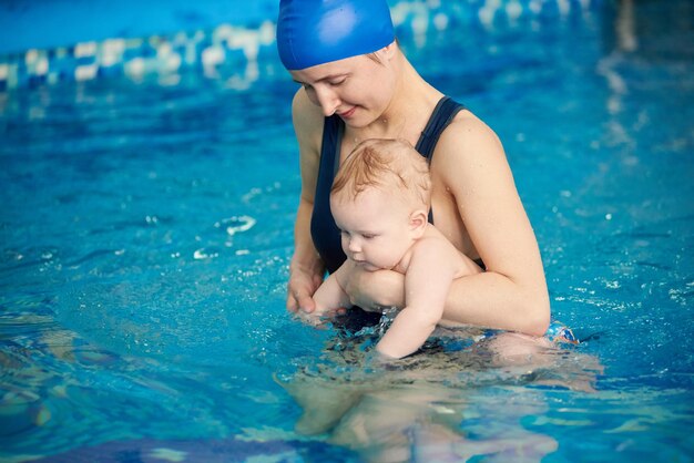 Młoda mama z dzieckiem podczas pierwszej próby pływania w basenie Pływanie w basenie dla harmonijnego rozwoju niemowląt