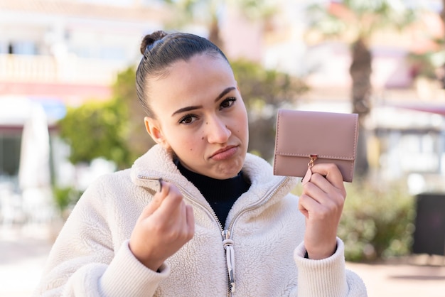 Młoda marokańska dziewczyna trzyma portfel na zewnątrz i ze smutnym wyrazem twarzy