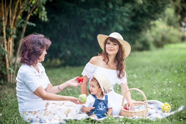 Młoda matka, babcia i synek bawią się na polanie. Piknik. Wiosna. Lato. Ciepło. Rodzina siedzi na trawie.