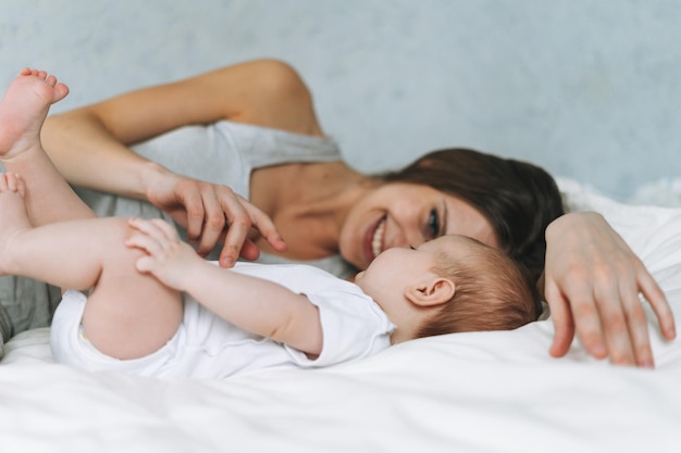 Młoda matka bawi się z uroczą córeczką na łóżku z białym lnianym naturalnymi odcieniami miłości