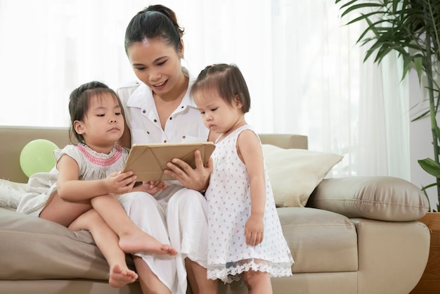 Młoda matka i jej dwie córeczki oglądają animowaną kreskówkę na tablecie w domu