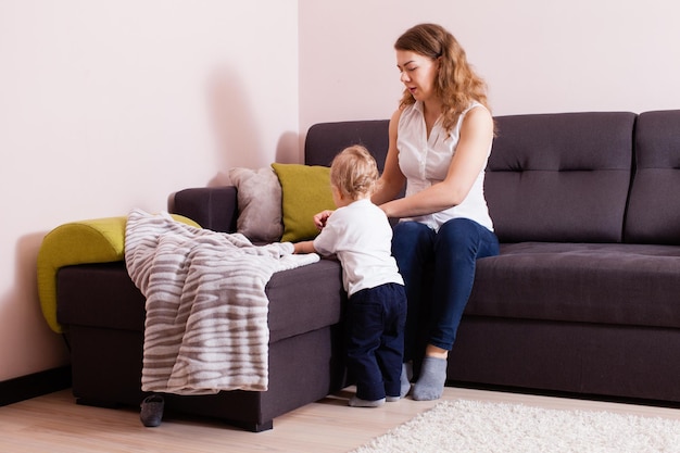 Młoda matka i jej maluch wchodzą ze sobą w interakcję w swoim domu. Młoda matka rozmawia z jej chłopcem, siedząc na kanapie.