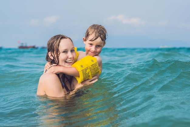 Młoda matka pływanie i gra z chłopcem dziecko w morzu lub ocean wody słoneczny dzień na świeżym powietrzu na tle naturalnego, poziomy obraz.