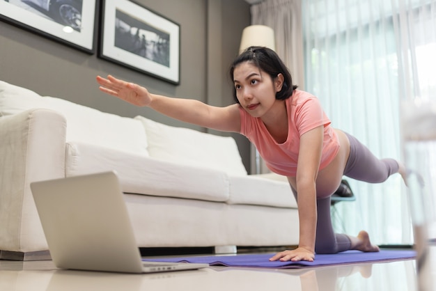 Zdjęcie młoda matka praktykuje jogę z klasą online na laptopie w pobliżu sofy