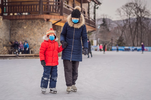Młoda matka uczy swojego małego syna łyżwiarstwa na lodzie na łyżwiarstwie zewnętrznym Rodzina nosząca maskę medyczną podczas COVID-19 koronowirus cieszy się zimą na łyżwiarstwie na świeżym powietrzu