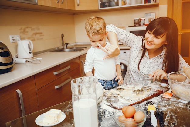 młoda matka w białej koszuli przygotowuje jedzenie w domu w kuchni z małym synkiem