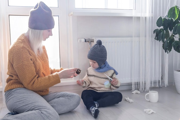 Młoda matka w żółtym swetrze mierzy temperaturę dziecka i podaje lekarstwo na chorobę