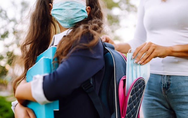 Młoda matka wkłada sterylną maskę do plecaka uczennicy. Życie podczas pandemii Covid-19.