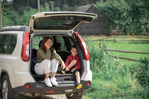 Młoda matka z dzieckiem chłopca siedzącego w bagażniku samochodu, odpoczywając w letnim słonecznym dniu koncepcji wycieczki samochodowej