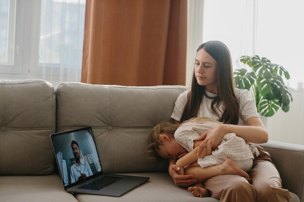 Zdjęcie młoda matka z małą córką konsultuje się z lekarzem rodzinnym za pomocą laptopa