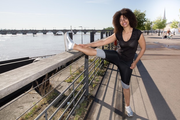 Młoda, mieszana czarna kobieta z kręconymi włosami rozciąga się po joggingu