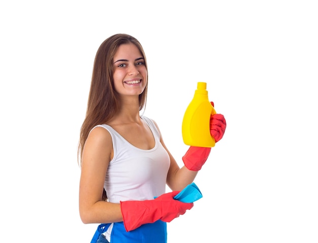 Młoda miła kobieta w białej koszuli i niebieskim fartuchu z czerwonymi rękawiczkami, trzymająca szmatkę i detergent