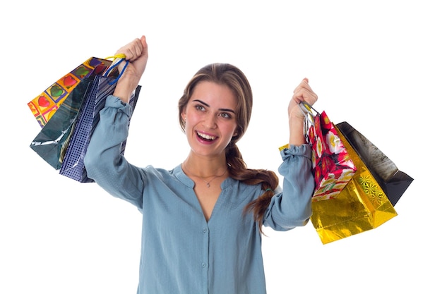Młoda miła kobieta w niebieskiej bluzce trzymająca torby na zakupy na białym tle w studio
