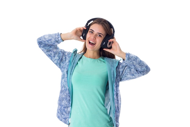 Młoda miła kobieta w niebieskiej koszuli słucha muzyki w czarnych słuchawkach na białym tle