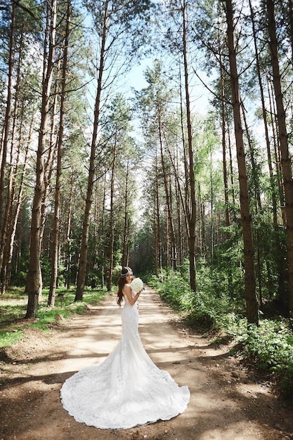 Młoda Modelka Kobieta W Stylowej Koronkowej Sukni ślubnej, Trzymając Bukiet I Pozowanie W Lesie.