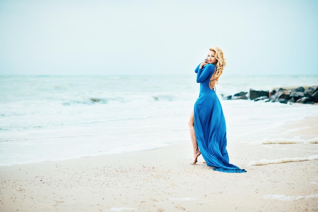 Młoda modelka w niebieskiej długiej sukience na brzegu
