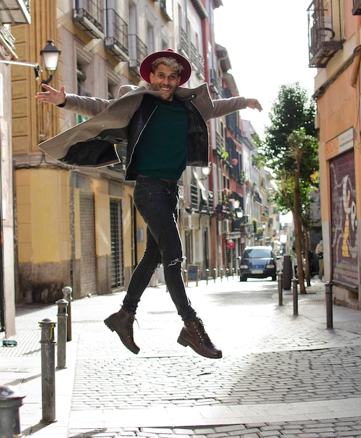 Młoda modelka w szarej kurtce i czerwonym kapeluszu skacze na ulicy