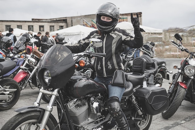 Młoda motocyklistka kobieta rocker w kasku motocyklowym siedzi na motocyklu i pokazuje gest kozy lub symbol skały gest dłoni CoolpartyszacunekKoncepcja zwycięstwa i chłodu