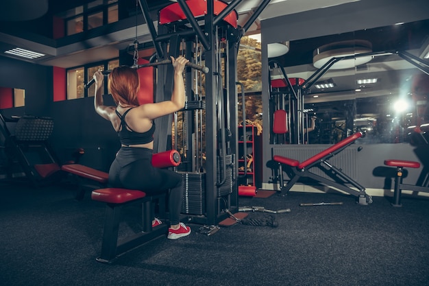 Młoda muskularna kobieta kaukaska ćwicząca w siłowni ze sprzętem wellness zdrowy styl życia