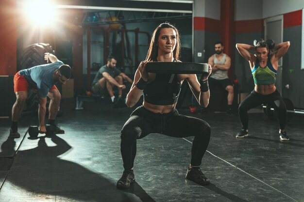 Młoda, muskularna, ładna kobieta robi ciężkie ćwiczenia z ciężkim talerzem na siłowni.