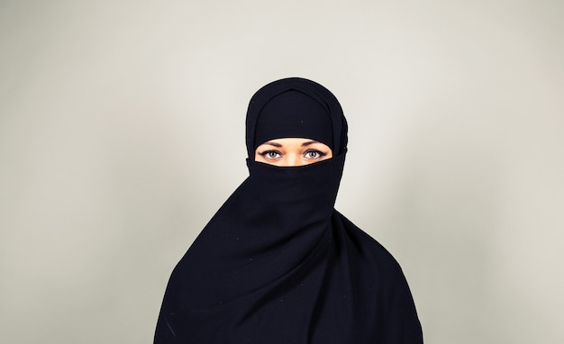 Młoda muzułmanka nosząca nikab na szarym tle