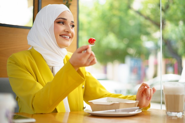 Młoda muzułmanka w hidżabie jedząca lunch w kawiarni