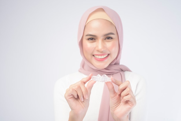 Młoda muzułmańska kobieta trzyma szelki invisalign na białym, opieki stomatologicznej i koncepcji ortodontycznej.