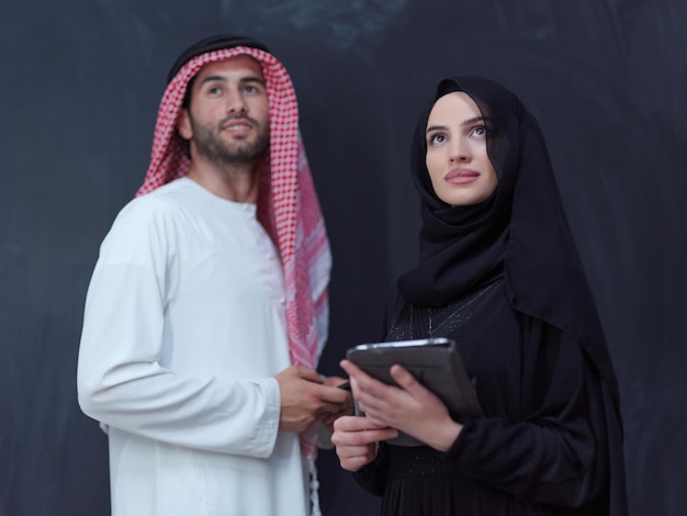 młoda muzułmańska para biznesowa arabski mężczyzna z kobietą w modnej sukience hidżabu za pomocą telefonu komórkowego i tabletu przed czarną tablicą reprezentującą nowoczesną technologię mody islamu i ramę