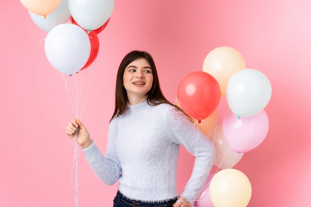 Młoda nastolatek dziewczyna trzyma mnóstwo balonów nad różową ścianą