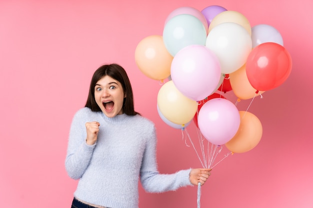 Młoda nastolatka dziewczyna trzyma mnóstwo balonów na różowej ścianie świętuje zwycięstwo